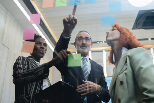 Diverse business team brainstorming ideas using sticky notes and digital tablet in modern office, teamwork and collaboration in creative planning session.