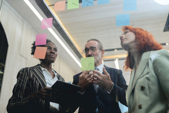 Diverse business team brainstorming ideas using sticky notes and digital tablet in modern office, teamwork and collaboration in creative planning session.