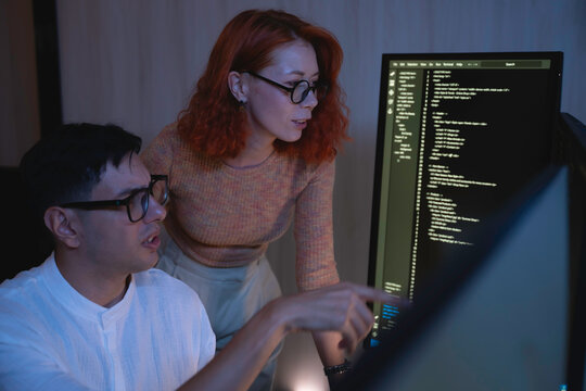 Two software developers collaborating at night, focusing on code review and debugging process on a computer screen, representing teamwork, innovation, and modern software development workflow. - Powered by Adobe