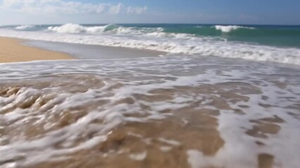 Ocean waves approach a sandy beach washing over tire tracks in the foreground