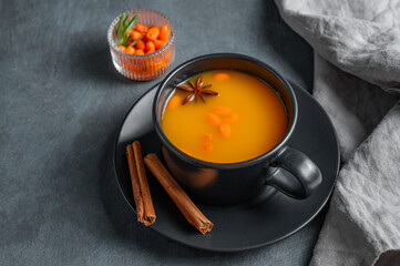 Sea buckthorn tea in a black cup on a dark background with berries, spices and napkin.