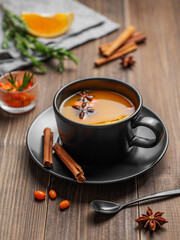 Sea buckthorn herbal tea in a black cup on a wooden background with spices