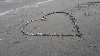 Close-up of a heart shape drawn in small pebbles on a textured gray concrete surface, roughness concept.