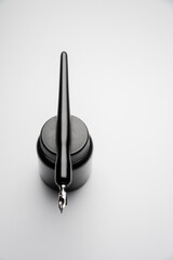 black ink bottle and a fountain pen resting on it, against a white background. Vertical photography, an aesthetic photo of old tools with a modern design