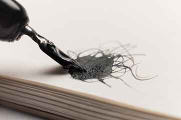 macro shot of a black abstract blob with lines and a fountain pen drawing the blob. A strange ink drawing
