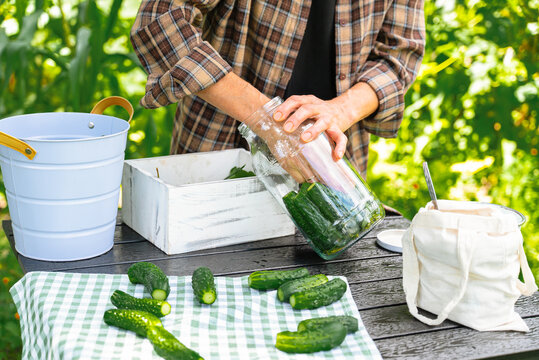 Hand placing fresh cucumbers into a large glass jar