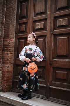 Little girl in floral dress holds pumpkin basket
