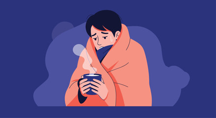 A sick young man wrapped in a warm blanket holds a mug of hot tea or coffee to help him feel better from a cold or flu.