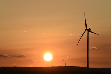 Obraz premium lever de soleil sur des éoliennes à contre-jour; ciel dégradé couleur bleue et orange avec des petits nuages cumulus blancs gris et noirs