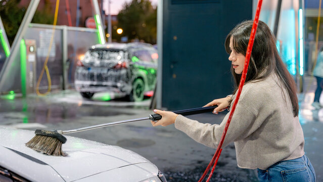 Woman cleaning car with pressure water at car wash station