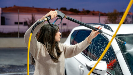 Woman using pressure washer for a car wash at sunset