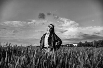 Stylish woman in black leather jacket and sunglasses poses confidently on urban sidewalk,...