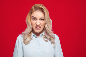 Aggressive young woman screaming, isolated on red background. Frustrated woman with grimacing face