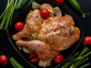 Whole raw chicken marinated with butter sauce and herbs added wRaw uncooked whole chicken marinated with herbs spices in soy sauce with butter lying in pan with red cheith red fresh tomatoes and leek.