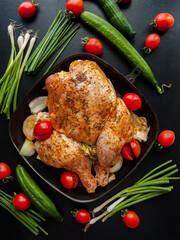 Raw whole chicken marinated with herbs and spices in soy sauce lying in pan with cherry tomatoes, cabbage and green leek onion ready to be cooked in oven. Dinner homemade meal chicken in preparation.