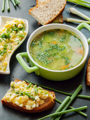 Healthy homemade chicken broth with boiled potatoes and egg salad sandwiches for cold days to keep warm and get proteins. Portion of bowl with hot tasty broth and baked whole wheat bread with salad.