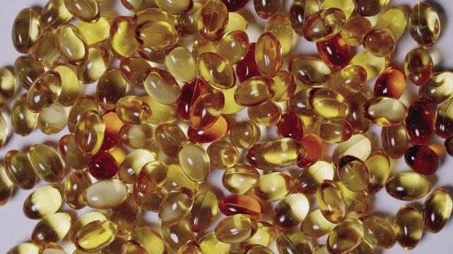 Top-down, close-up video of golden softgel capsules, like vitamin or fish oil supplements, slowly rotating on a turntable on white background showing concepts of healthcare, medicine, and nutrition.