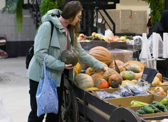 In a vibrant marketplace, a young woman with a blue shopping bag pauses in front of a display of...