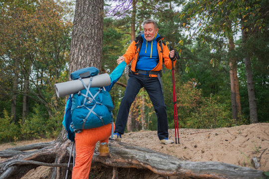 Hiking adventure. Man helping hand woman on hiking in forest. Senior couple enjoying outdoor recreation hiking. Happy old people backpackers hikers enjoy walking hike trekking tourism active vacation