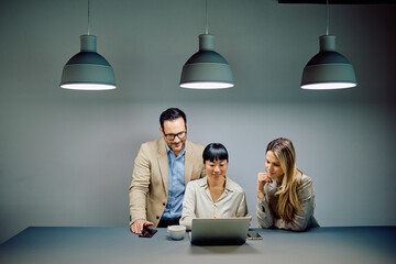 Diverse business professionals working together, discussing ideas, and analyzing data on a laptop in a contemporary workspace