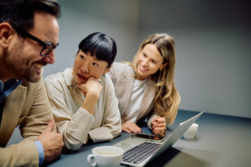 Business colleagues working together, discussing ideas and planning projects around a laptop and coffee cups in a modern office setup