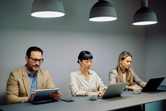 Diverse businesspeople focused on work, using laptops and tablets in a modern office, representing technology integration and productivity
