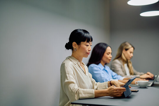 Diverse businesswomen concentrating on their digital devices, collaborating in a modern coworking space. Focus on technology and professional environment - Powered by Adobe