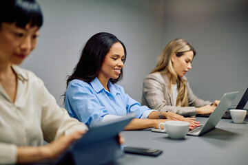 Diverse businesswomen attending a meeting, networking, and working on laptops and tablets in a modern corporate office environment