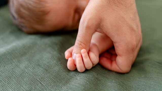 Tiny baby hand holding adult finger on soft green fabric - Powered by Adobe