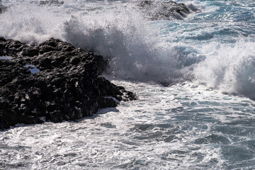 Powerful ocean waves crashing against black volcanic rocks on the coast of Tenerife. Dynamic seascape with white foam and textured lava cliffs.