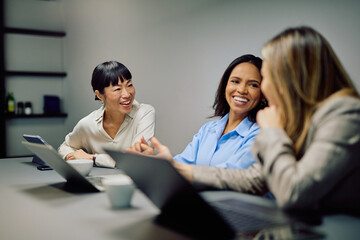 Diverse businesswomen collaborating and sharing ideas during a relaxed in-office meeting, showing teamwork and positive communication