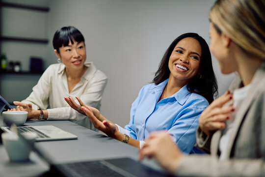Multiracial businesswomen collaborating, discussing, and smiling during a professional meeting in a modern office environment