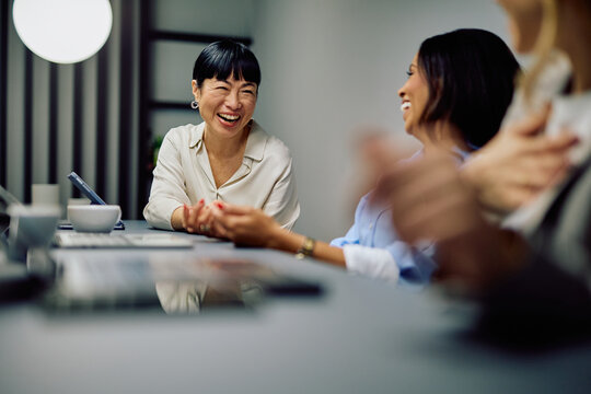 Smiling businesswomen having a conversation, sharing a laugh during a casual office meeting, showing teamwork and joy