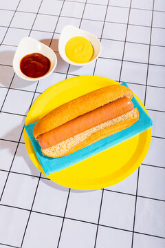 Hot dog on yellow plate with condiments in dishes