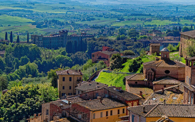 Obraz premium Aerial view of Siena’s rooftops and Villa il Pavone, where terracotta tiles, and Tuscan greenery blend into a timeless cityscape. Harmony between heritage and natural beauty from above.