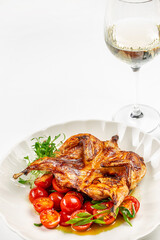 Grilled quail with cherry tomatoes and fresh herbs served on a white plate with a glass of white wine, copy space premium culinary advertising
