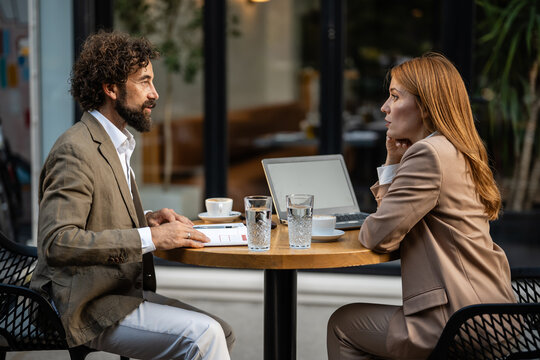 Business people discussing at outdoor cafe table with laptop and documents
