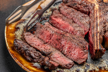 Juicy medium rare grilled T-bone steak sliced on plate with steak knives, close-up of tender beef meat with seasoning and juices