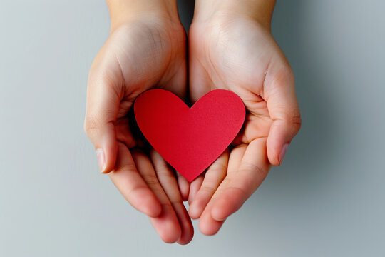 hands gently holding small red paper heart shape, concept of love, health, donation, care and sharing