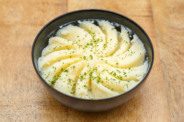 Purée de pommes de terre dans un bol noir. Table en bois. 