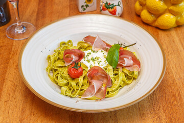 Tagliatelles au pesto avec jambon de Parme, tomates confites et basilic sur une table en bois