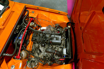 Classic car engine bay showcases detailed mechanics of vintage vehicle with bright orange paint during motorsport event