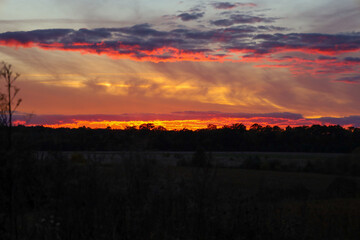 Obraz premium This is an enchanting sunset landscape, painting the sky with fiery hues of orange, red, and gold, featuring dramatic clouds that underscore the moment's majesty.