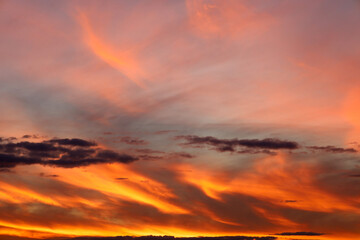 A vibrant sunset paints the sky with dramatic shades of orange, red, and pink. Cirrus and stratus clouds are illuminated by the fiery light, creating a captivating and dynamic natural landscape.