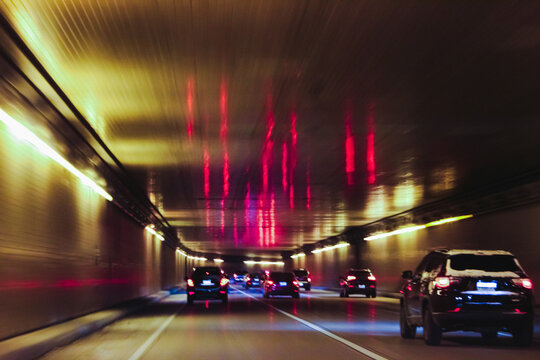 Traffic moves through a bridge tunnel, with striking red ceiling reflections. Urban transportation design element or background with blurred effect.