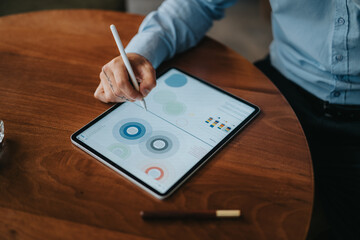 A person interacts with a tablet using a stylus, displaying circular charts and data visuals.