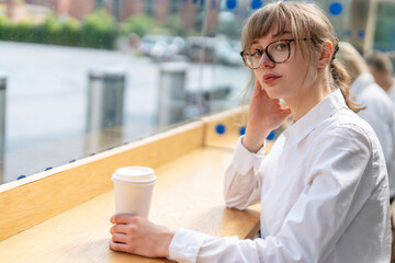 Young woman sitting at café window with coffee in hand on a sunny day