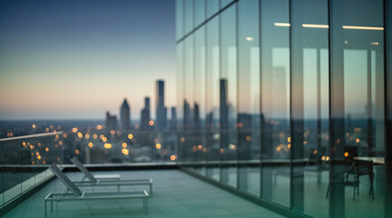 A blurred view of a modern city skyline at dusk from a high-rise balcony with glass railings and lounge chairs.