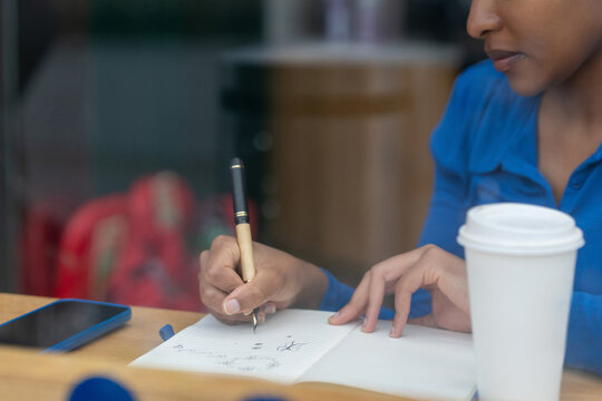 Person writing in notebook with coffee cup and smartphone nearby in a modern setting - Powered by Adobe