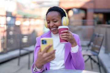 Woman enjoying coffee and music while using smartphone outdoors at a social gathering